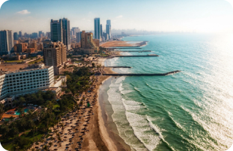 Aerial coastal city view with high-rises, beach, and waves, featuring sweet water tanker supply under a bright sky.