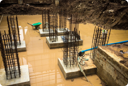 Construction site with multiple steel rebar columns set in concrete bases, showing preparation for building work and supported by water for piling sites.